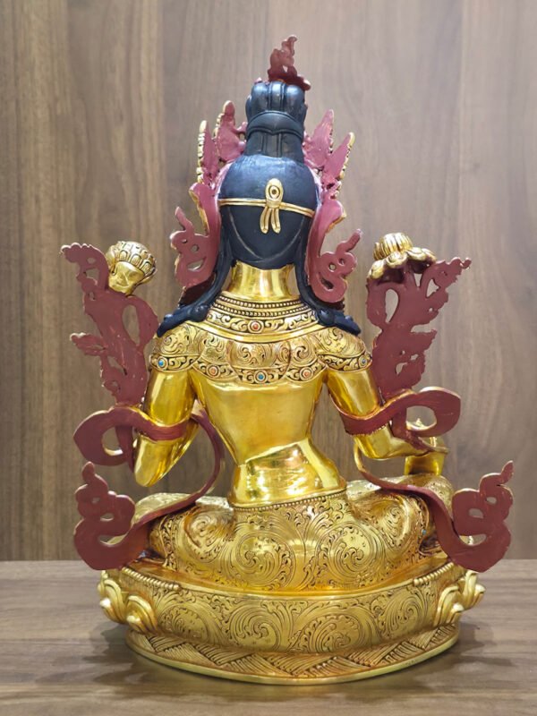 Rear view of the gold plated Green Tara statue showing dark painted hair, engraved garments and lotus base against a wood background.
