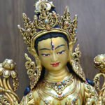 White Tara statue face and crown close-up, showing the gold powder painted face, forehead eye, red coral and blue lapis lazuli accents