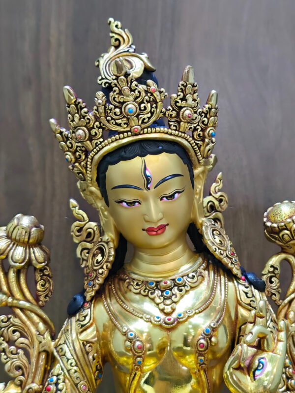 White Tara statue face and crown close-up, showing the gold powder painted face, forehead eye, red coral and blue lapis lazuli accents