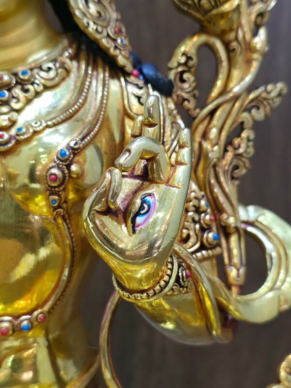 Seven-Eyed White Tara statue in 24K gold plated copper, close-up of the painted eye on the raised left palm beside a lotus stem.