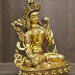 White Tara statue in 24K gold plated copper, right-facing angled view with lotus flowers and a lotus pedestal against a wood background.