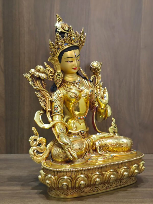 White Tara statue in 24K gold plated copper, right-facing angled view with lotus flowers and a lotus pedestal against a wood background.